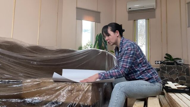 A beautiful young woman engages in home improvement, planning preparing for renovation on backdrop of construction materials indoors. Reconstruction, DIY concept. Handywoman makes remodeling plan