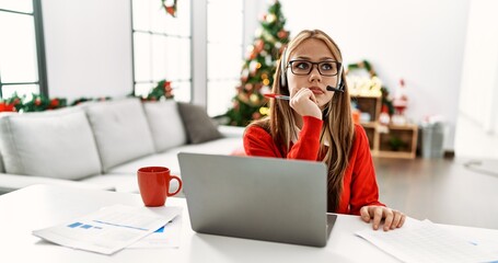 Young caucasian woman call center agent teleworking sitting by christmas tree at home