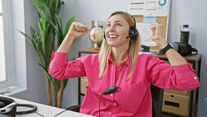 A joyful caucasian woman celebrates success with headphones in a modern office setting