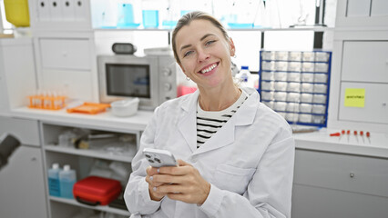 Fototapeta na wymiar Smiling woman in lab coat using smartphone in a modern laboratory setting