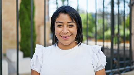 Smiling middle-aged hispanic woman in a white shirt posing outdoors with a blurred park background.