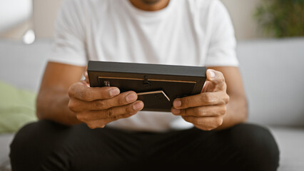 Young hispanic man examines portrait indoors, providing a sense of home and personal reflection.