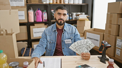 A young bearded man holding money volunteering at an indoor donation center. - obrazy, fototapety, plakaty
