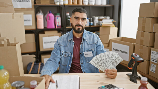 A young bearded man holding money volunteering at an indoor donation center.