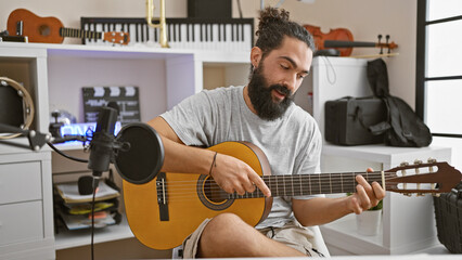 Hispanic man playing guitar in a home music studio with microphone and musical instruments