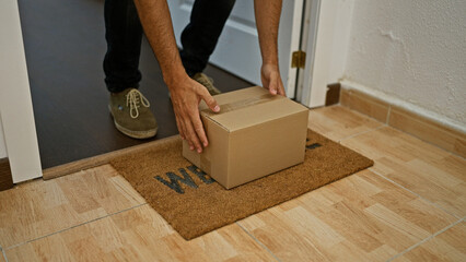 A young man picking up a cardboard box from a welcome mat in a home interior, showcasing a casual...