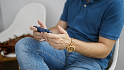 Fototapeta na wymiar Mature hispanic man using smartphone in a modern indoor room, wearing casual clothing and a wristwatch.