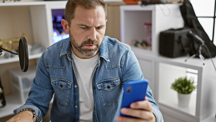 Handsome middle-aged man with grey hair focused on smartphone in modern indoor studio setting.