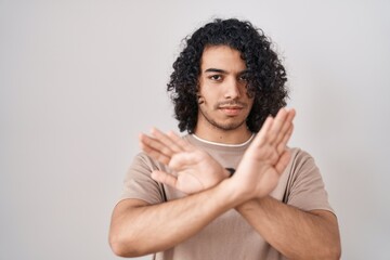 Hispanic man with curly hair standing over white background rejection expression crossing arms and...
