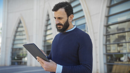 A middle-aged man with a beard looks at a tablet on a city street.