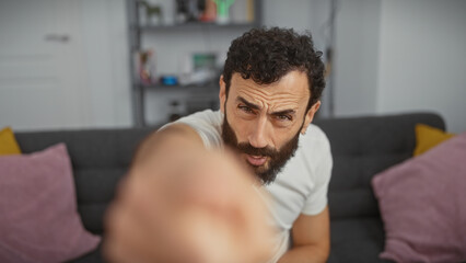 Obraz premium Handsome middle-aged man with beard extending hand towards camera in modern living room.