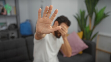 A man shows refusal gesture in a modern living room, conveying privacy, rejection, or boundary...