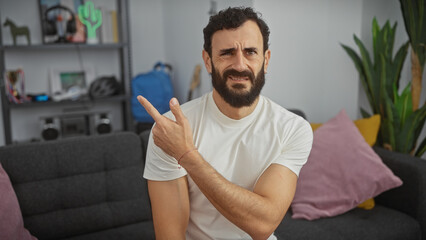 A confused bearded man pointing in his modern living room.