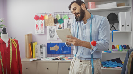 A bearded tailor in a blue shirt multitasks, talking on the phone while examining notes in a...
