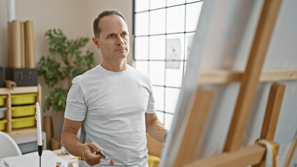 Handsome middle-aged hispanic man concentrating on drawing artwork in vibrant art studio