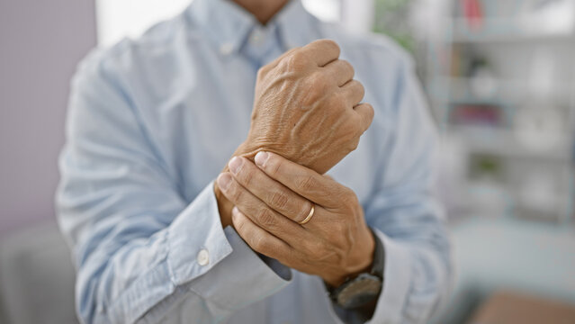 At home, a cool-looking middle age man, in his living room, suffering intense wrist pain, an alarming adult problem, fights hard against this troublesome joint injury.