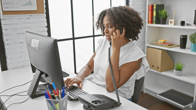 African american woman with braids making a phone call and using a computer in an office