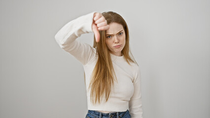 A disappointed young woman giving a thumbs down gesture against a white background expresses...
