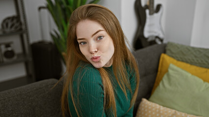 Naklejka premium A young caucasian woman with blonde hair wearing a green sweater poses playfully indoors on a cozy sofa, pouting for the camera.