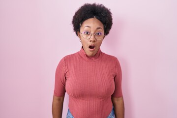 Beautiful african woman with curly hair standing over pink background afraid and shocked with surprise and amazed expression, fear and excited face.