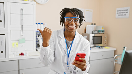 Young african american woman with dreadlocks and lab coat in a laboratory, smiling while holding a...