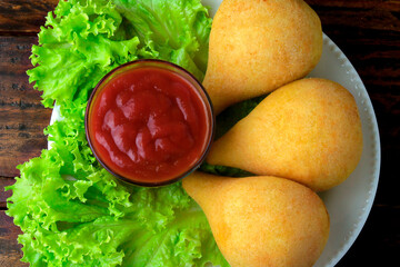 Coxinha in the dish, traditional Brazilian cuisine snacks stuffed with chicken, on rustic wooden table