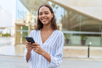 Young african american woman smiling confident using smartphone at street