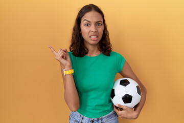 Young hispanic woman holding ball pointing aside worried and nervous with forefinger, concerned and...