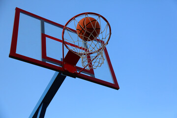 A basketball ball flies into a basket on a street basketball court.