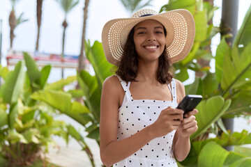 Young african american woman wearing summer hat using smartphone at park