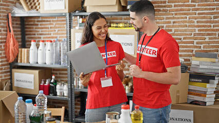 Volunteers cheer, man & woman celebrating win at the charity center, standing confident with laptop...