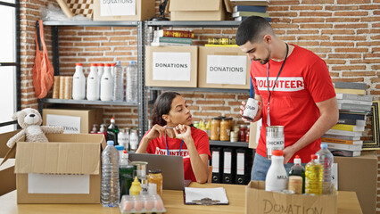 Two dedicated volunteers, a young man and woman, vigilantly checking charity donations online via...
