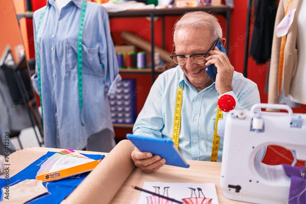 Poster middle age grey-haired man tailor talking on smartphone using touchpad at atelier