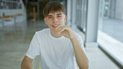 Caucasian teenage boy smiling in university library wearing white shirt sitting at table.