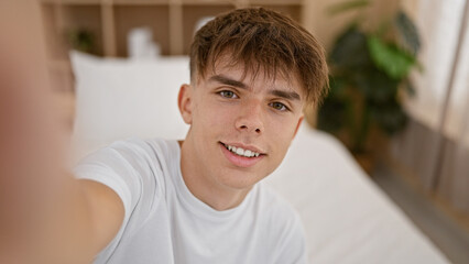 Caucasian teenage boy with blond hair taking a selfie in a bedroom with a modern interior design. © Krakenimages.com