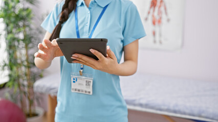 Asian woman healthcare professional using tablet in clinic interior, embodying modern medical practice.