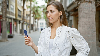A contemplative young woman holding a card on a palm-lined urban street.