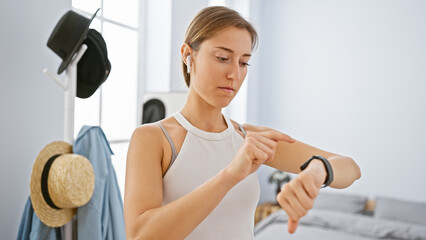A young woman checks her smartwatch in a modern bedroom, indicating an active and technology-driven...
