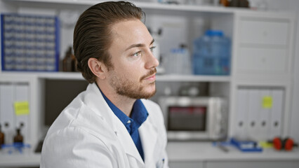 Young hispanic man scientist sitting on chair relaxed at laboratory