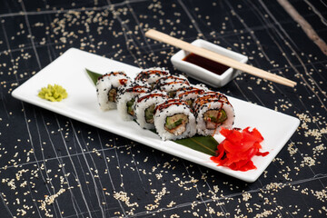 Set of sushi rolls dragon on a black matte plate. Japanese traditional sushi dish with avocado, eel and soy sauce. A beautiful dish for an Asian restaurant menu.