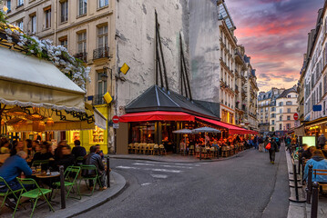 Cozy street with tables of cafe in Paris, France. Architecture and landmark of Paris. Sunset cozy Paris cityscape.
