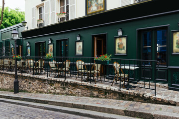 Fototapeta na wymiar Cozy street with tables of cafe in quarter Montmartre in Paris, France. Cozy cityscape of Paris. Architecture and landmarks of Paris.