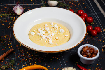 Banush or banosh is a Ukrainian dish prepared from cornmeal with cream topped with bacon, onion and bryndza closeup on the bowl on the wooden table. Vertical top view from above