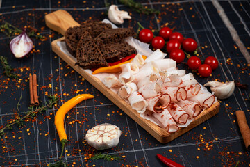 Homemade salted lard, slices with garlic and black pepper on wooden board. Dark background. Top view.