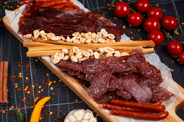 Top view of hands clanging glasses of beer together, near big wooden tray with delicious snacks, on wooden background