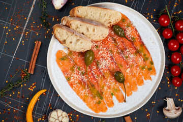 Salmon carpaccio with herbs, on a plate, on a dark background