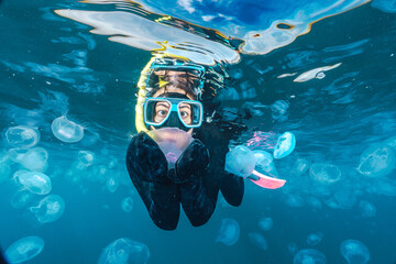 A woman is swimming in the ocean with jellyfish in the water
