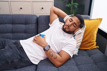 Young latin man listening to music sleeping on sofa at home