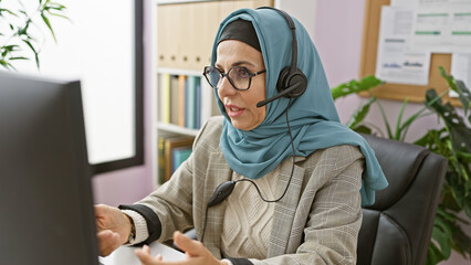 Professional woman wearing hijab using headset in modern office setting