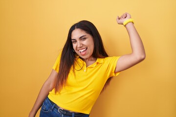Young arab woman standing over yellow background dancing happy and cheerful, smiling moving casual and confident listening to music